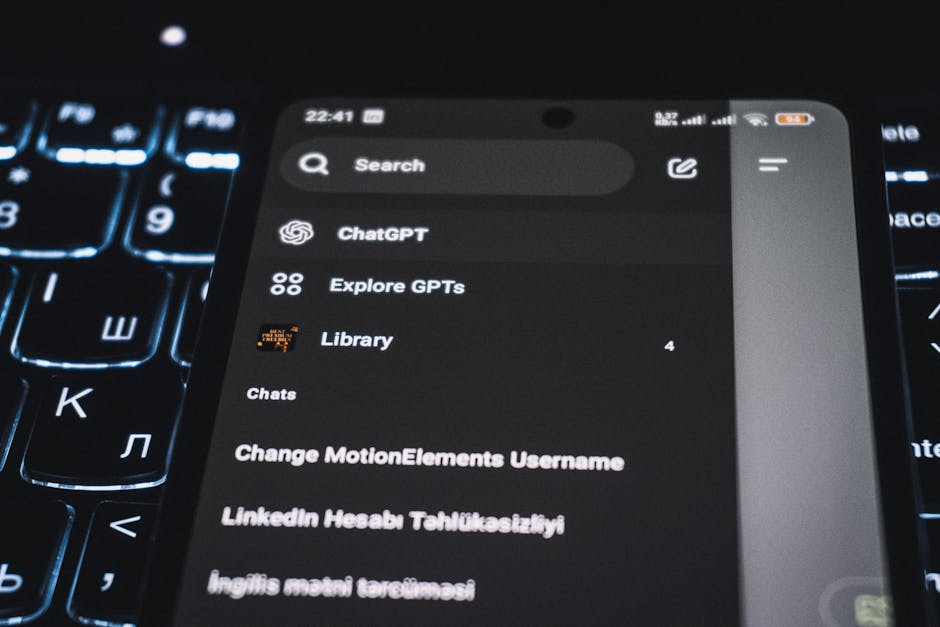 Close-up of a smartphone displaying a chat app interface with a backlit keyboard in the background.