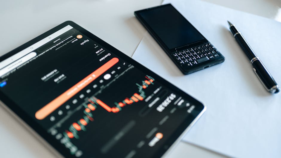 Close-up of a tablet displaying financial graphs, a smartphone, and a pen on a table.