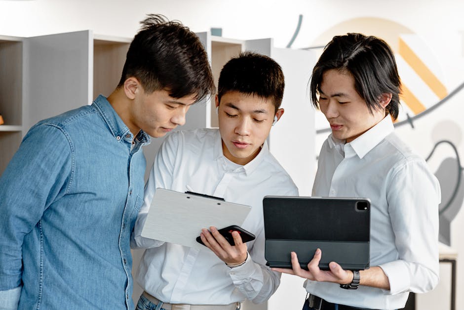 Three young professionals engage in discussion over digital tablets and documents in a modern office setting.